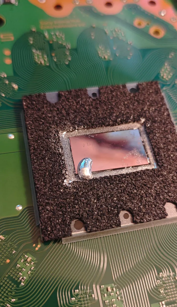 PS5 processor cleaned to a mirror finish, with a small bead of fresh liquid metal on its surface