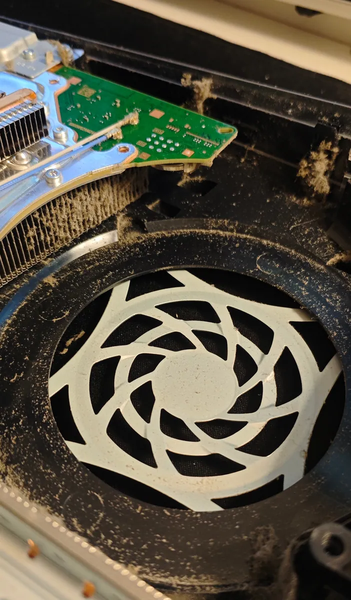 Inside the PS5 with the cover off, dust lining the fan opening and clinging to the edge of the heatsink