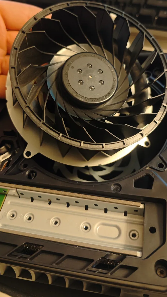 The PS5 fan held above the console after cleaning, with clean black blades and hub