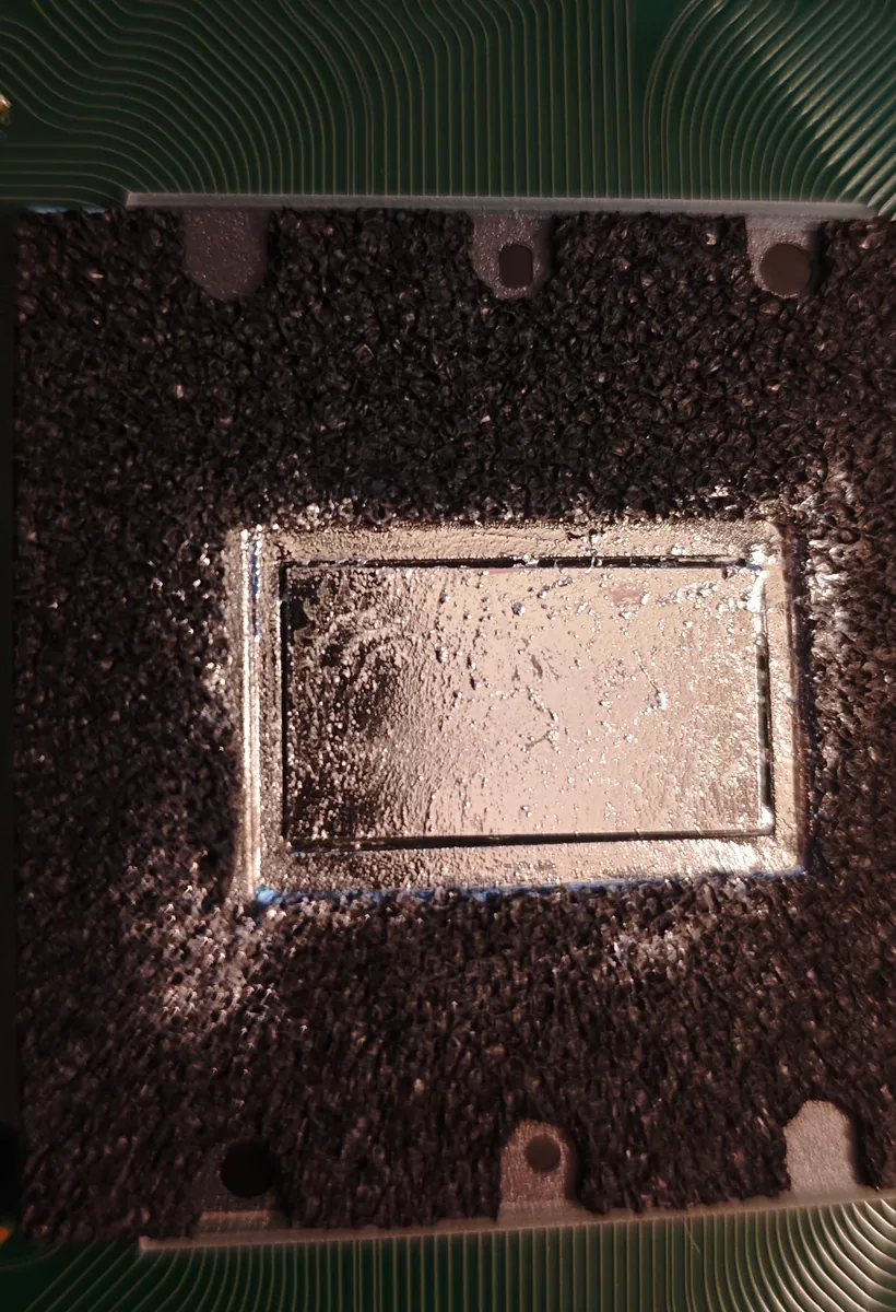 Fresh liquid metal spread in a thin, even layer across the PS5 processor, inside the foam barrier around the chip