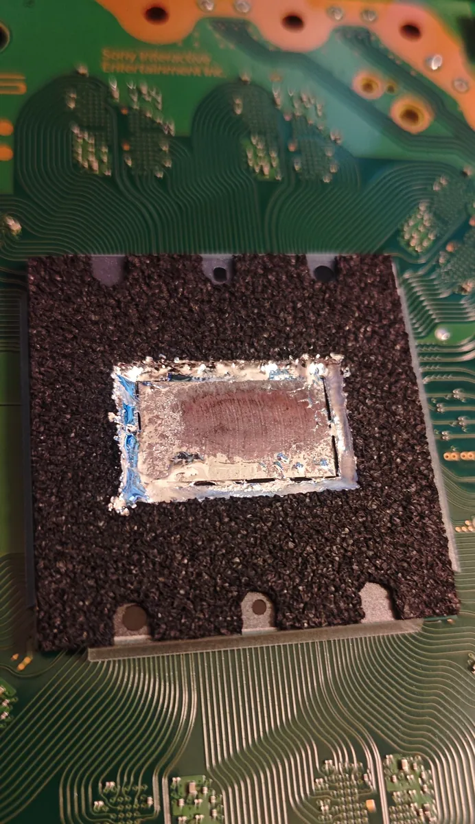 PS5 processor with the heatsink removed: old liquid metal pushed to the edges of the chip and a dull grey layer in the middle, inside a black foam barrier