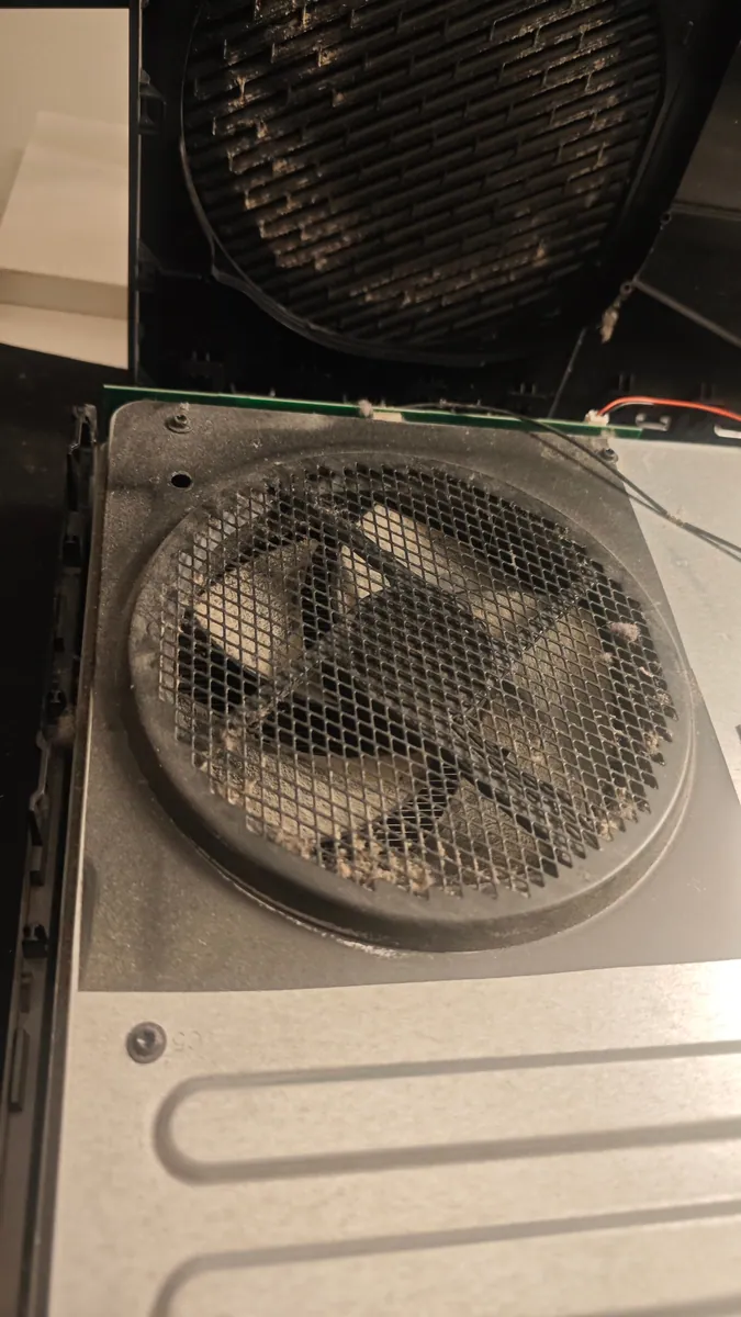 Xbox One opened up, with dust clogging the metal mesh above the fan and the vent grille in the top cover
